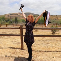 This is a picture taken of a woman in graduation clothing, posing for a photo in a desert landscape. 