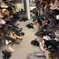 This is a picture taken of a messy footwear isle at a store. Shoes lie strewn across the ground of the isle. 