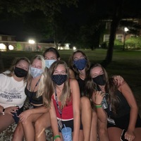 This is a picture of a group of six women wearing face masks, who are posing and smiling for the camera in an outdoor setting. 