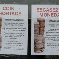 Two signs, one in Spanish and one in English, detailing a coin shortage. 