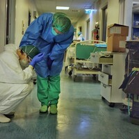 A distressed healthcare worker on the floor in a hospital being comforted by another healthcare worker.