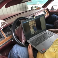 A photo of two people in a car, using a computer for a Zoom meeting.