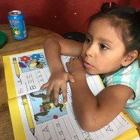 This is a picture of a young girl resting her elbows on her spelling homework, which lays on the table in front of her. 