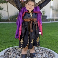 A girl poses in her costume in front of a tree with "Happy Birthday" banner.