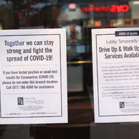 Two window signs from New York Community Bank. The first sign says "Together we can stay strong and fight the spread of COVID-19. If you have tested positive or await test results for Coronavirus (COVID-19) please do not enter the branch location. Call (877) 786-6560 for assistance."
The second sign says "COVID-19 Update. Lobby temporarily closed. Drive up & walk up window services available only. In our continuing effort to keep our services available while protecting the health and safety of our employees, customers, and communities, this branch lobby will be closed and this branch will operate the walk up and drive up windows only, until further notice. Our ATMs, customer contact center, online banking, mobile banking, and telephone banking services remain available for your banking needs. Please visit myNYCB.com for information on how you can conduct your banking safely, securely, and conveniently from virtually anywhere 24/7 or call us at (877) 786-6560 for assistance."