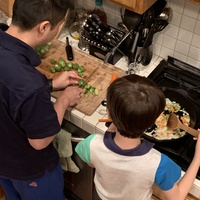 This is a picture of a man and his young son preparing dinner at a stove. 