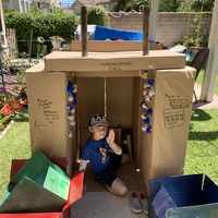 A child sitting in a cover made of cardboard boxes.