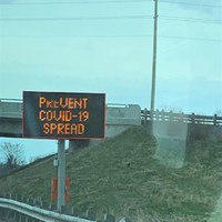 Image of a sign on the side of the highway which reads prevent Covid-19 spread.