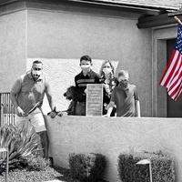 A family poses in front of a house with an American flag. 