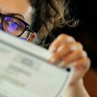 Picture of a female poll worker wearing a mask carefully looking at a document. 