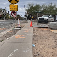 This is a picture of a discarded face mask that has been left near a sidewalk. A railroad crossing, several cars, and some buildings can been seen in the background. 