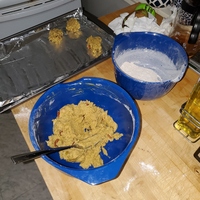 Two blue mixing bowls with baking ingredients. In background is a baking sheet lined with foil with dollops of dough.