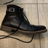 This is a picture of a leather shoe with laces and a buckle resting lengthwise on a tile floor. 