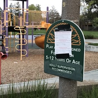 A public notice is taped over a sign to a playground. 