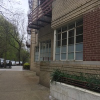 Brick buildings to the right of a walkway bordered by cars on the left.