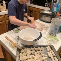 This is an image of a man who is flattening dough with a rolling pin to use in cooking. 