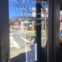 The glass front door of a café that has the hours written on it. 