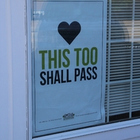 A sign in a window reading "This too shall pass".