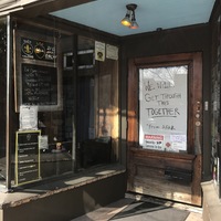 The front of a brown entrance with a glass door. On the inside of the glass door says: WE WILL GET THROUGH THIS TOGETHER *FROM AFAR.