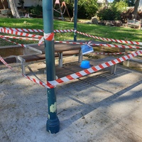 Photo of a park. All seating areas and playground equipment are blocked off with ted and white tape.