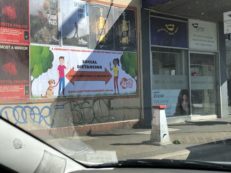 The side of the building that has numerous advertisements and signs about social distancing. Below the advertisements is blue and black graffiti. 