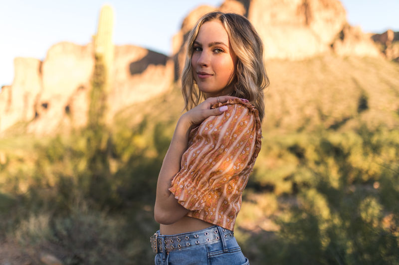 A person posed for their high school senior photo in a desert landscape. 