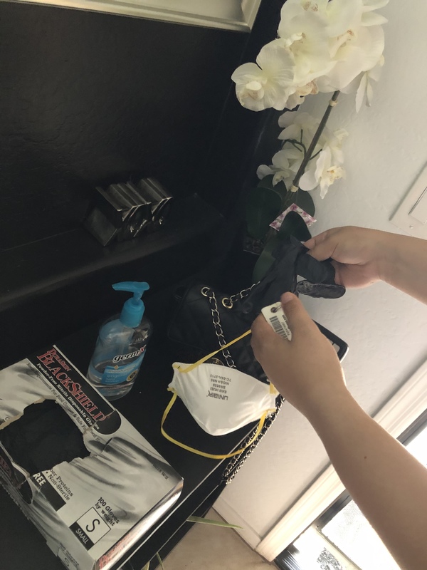 A bottle of hand sanitizer next to a purse and a mask. 