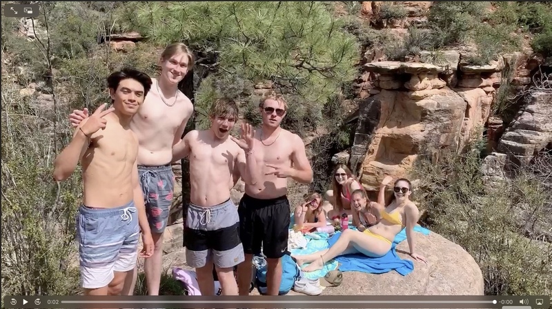 Four people in front standing and four people in back sitting on towels on top of a rock with large rock formations in the background. 