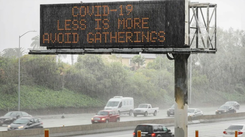 Highway sign that says "COVID-19, less is more, avoid gatherings."