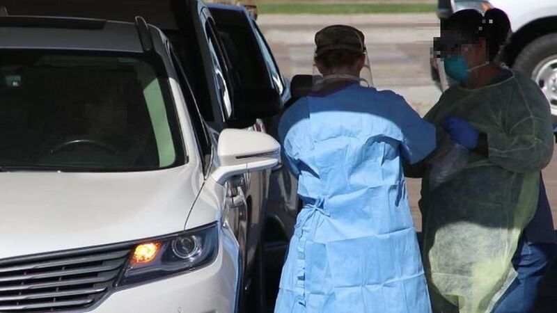Two people in protective gear working at a drive through COVID-19 testing site in Iowa. 