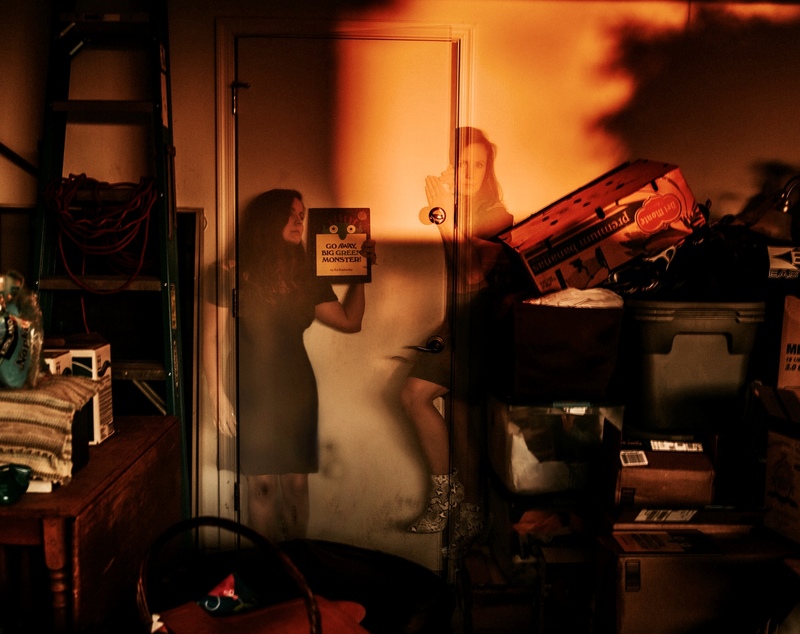 A person is holding a book up that says: "Go away, big green monster!" Another person has half their body inside of the room and outside of the room. 